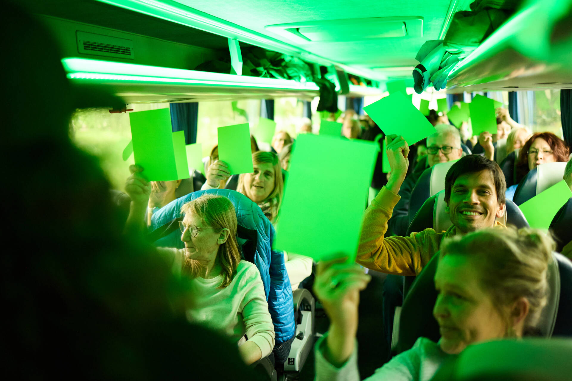 Eine Reisegruppe hält im Bus grüne Karten hoch