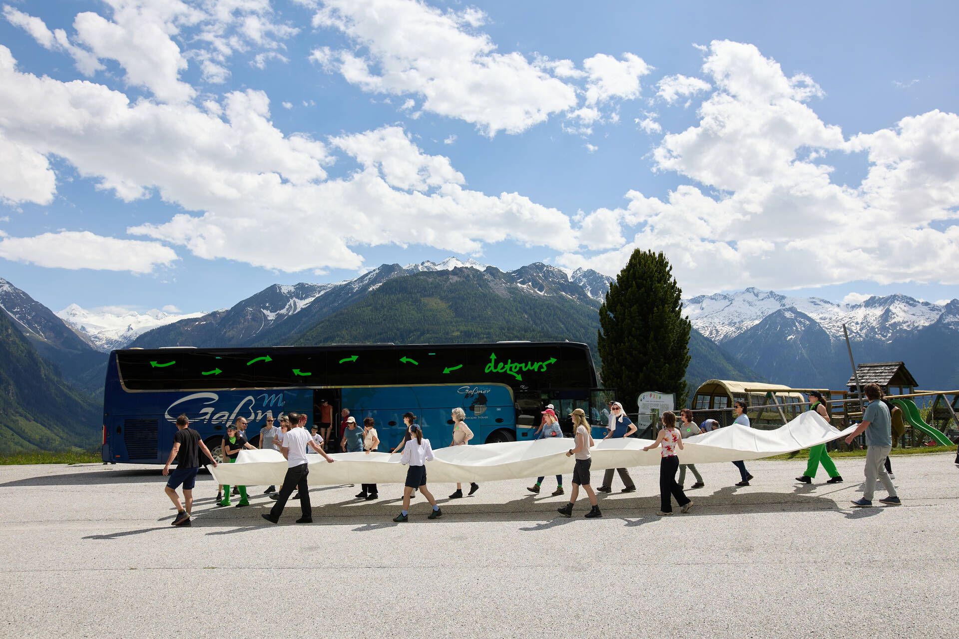 Die Gruppe trägt ein großes weißes Tuch, der Bus im Hintergrund
